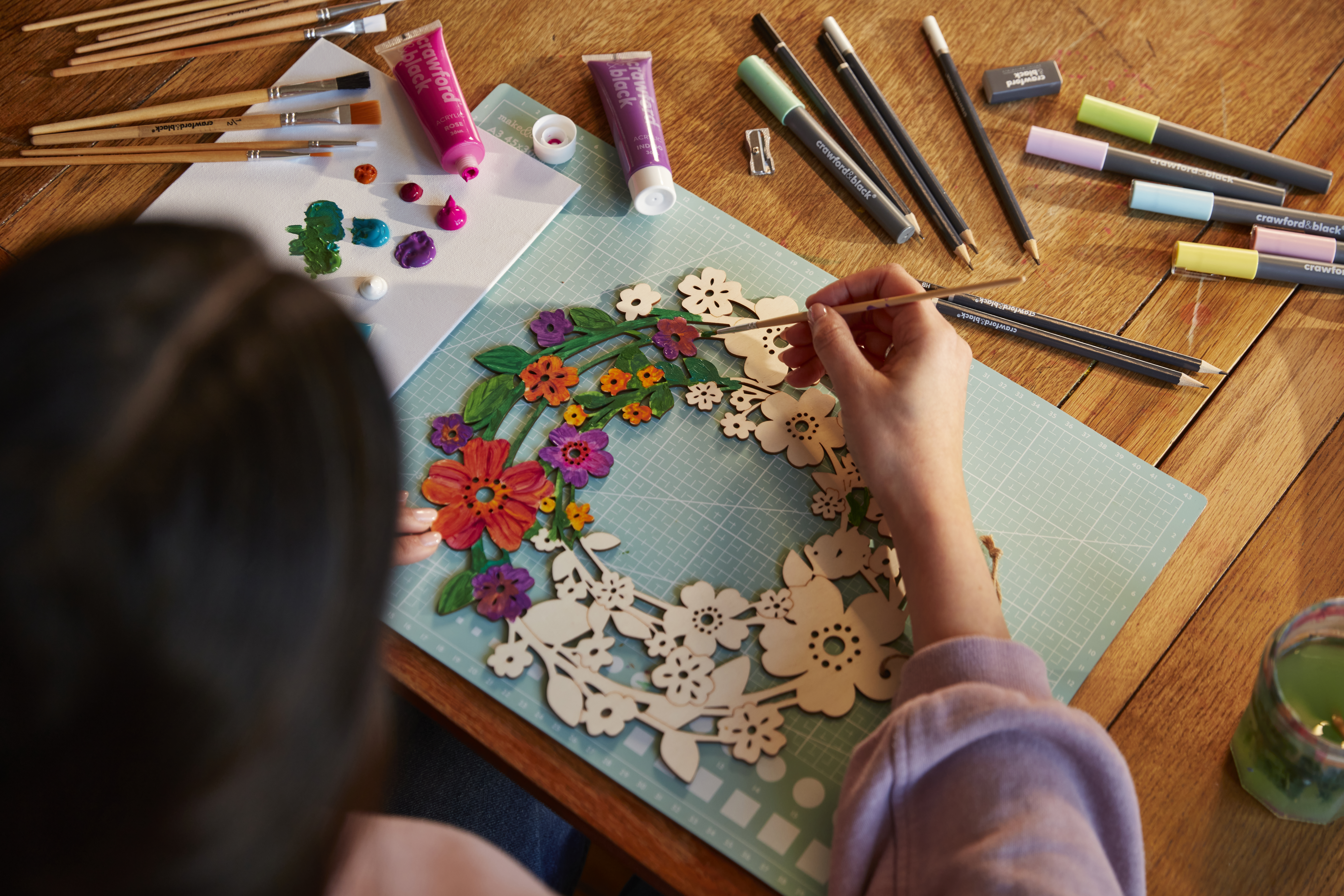 Benefits of crafting for wellbeing: painting. Bird's eye shot of someone painting a wooden floral wreath.